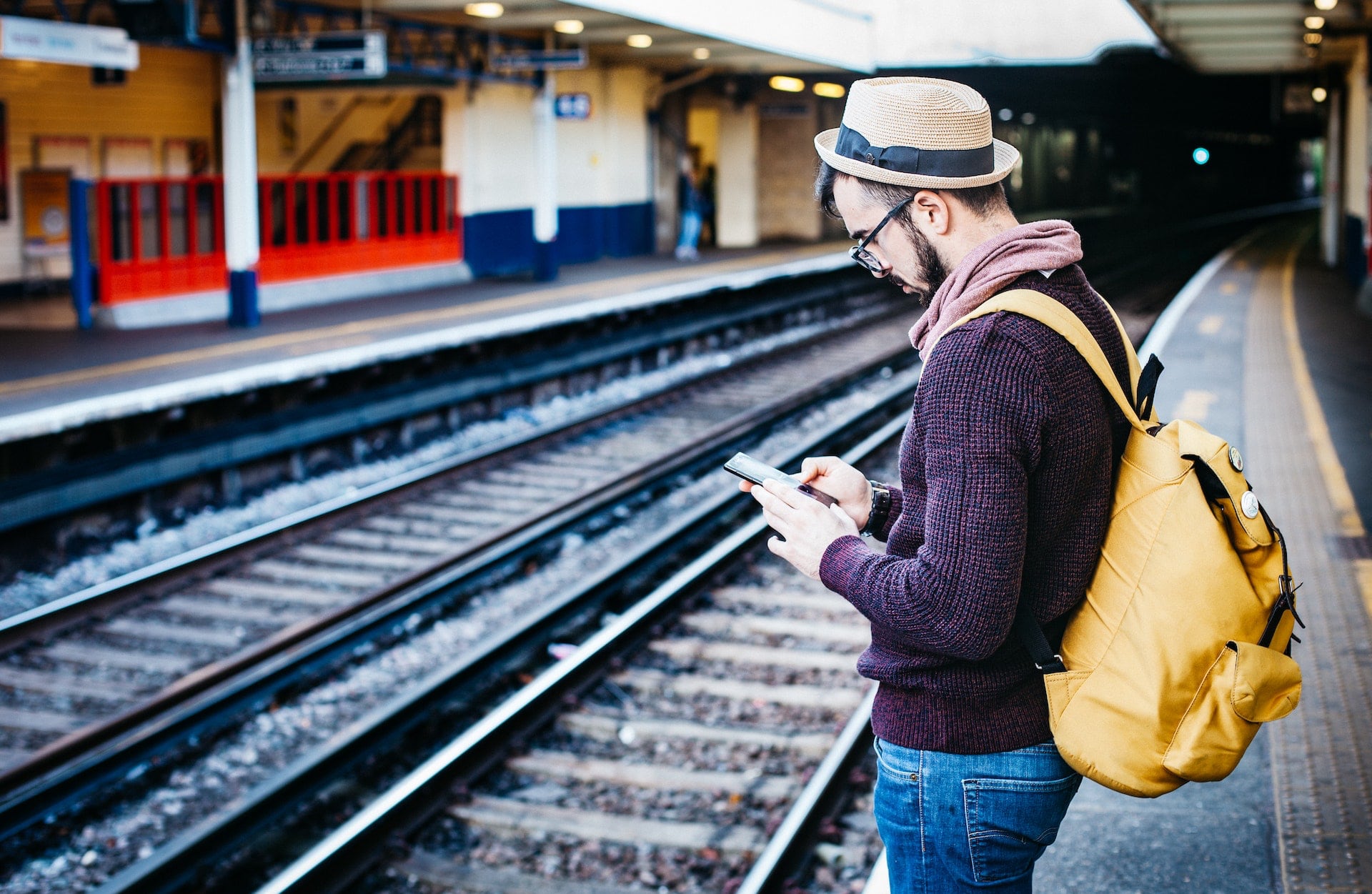 A photo of a man on his phone, standing on a train station platform